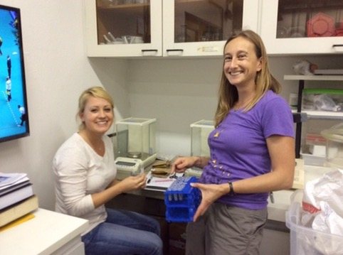 Two researchers smiling at a lab bench with balances and sample racks