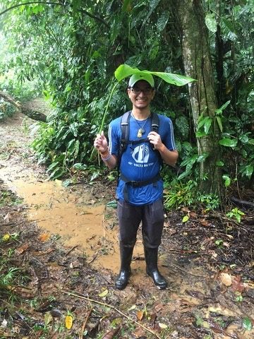 Student holding a large leaf over his head on a muddy trail